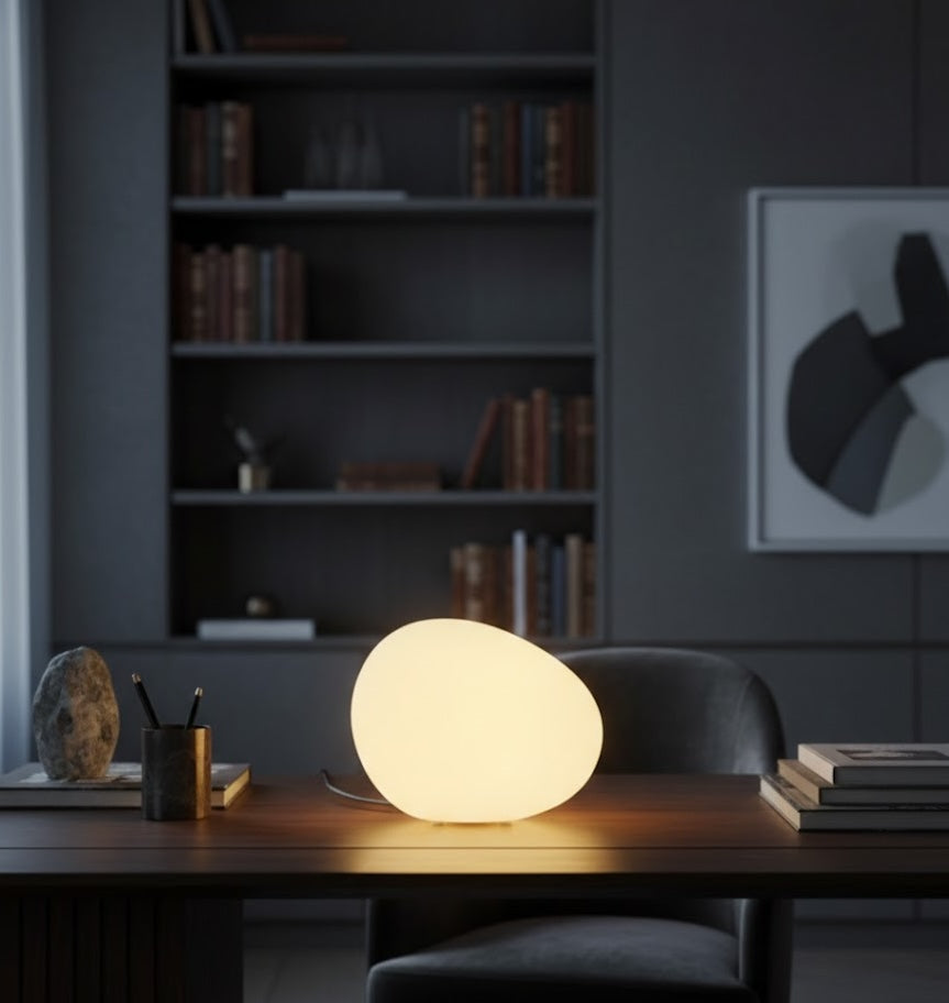 Round table lamp on a desk with a bookshelf and framed picture in the background