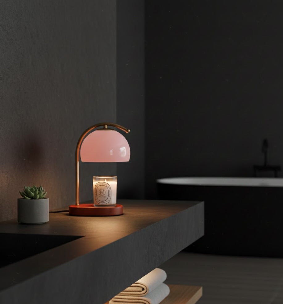 Pink table lamp on a wooden surface with a candle and small plant in a dark room.